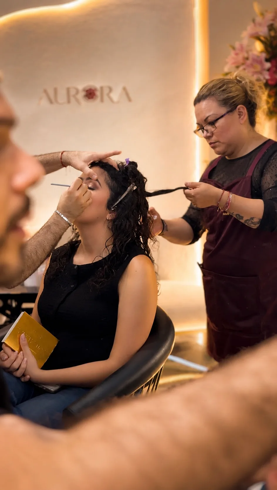 Dos personas del equipo trabajando al mismo tiempo sobre una clienta: maquillaje y peinado.
